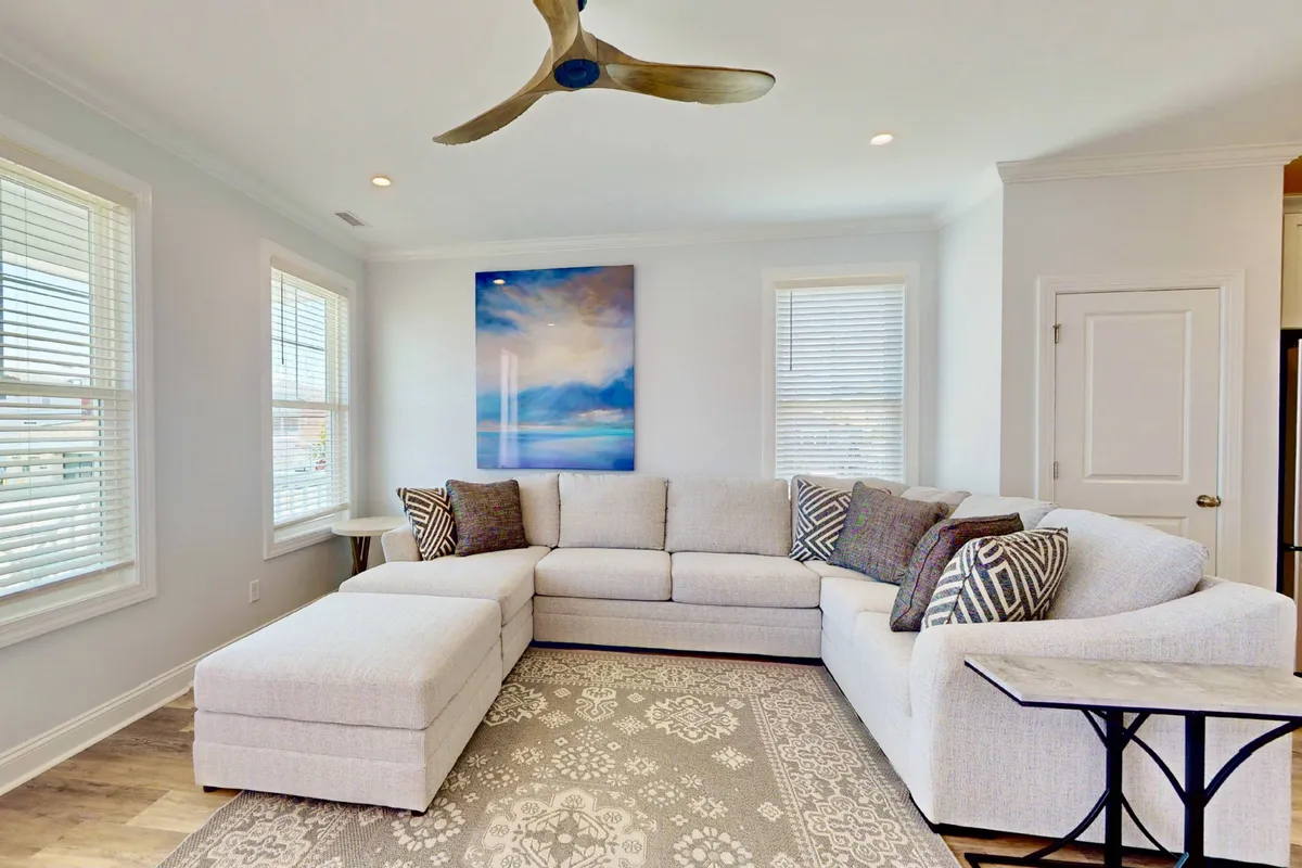 A large sectional sofa anchors a cozy living room, complemented by an abstract painting and decorative pillows. The area feels warm and communal, perfect for relaxing, watching movies, or sharing stories with loved ones.