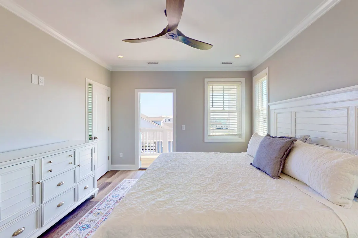 A tranquil bedroom with a comfortable bed positioned near a window, a dresser, and a ceiling fan overhead. Natural light streams into the room, creating a peaceful and airy atmosphere that emphasizes comfort and relaxation.
