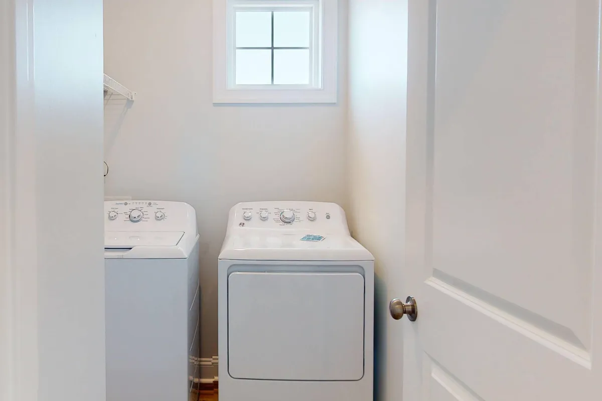 A tidy laundry area featuring a washing machine and dryer beneath a window, exuding practicality and cleanliness. Natural light brightens the space, creating an inviting spot for handling chores with ease.