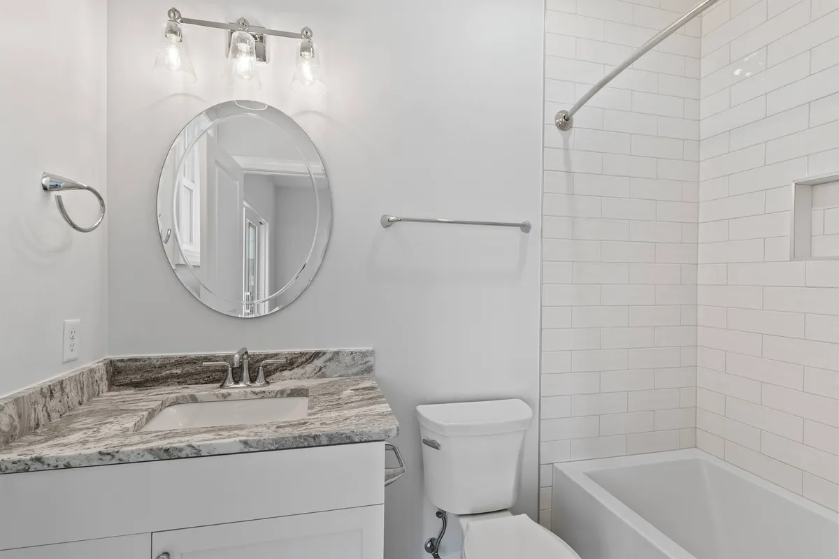 A calming bathroom scene with a granite countertop, round mirror, bright lighting, and a bathtub. The atmosphere is serene and welcoming, ideal for unwinding after a long day by the sea.