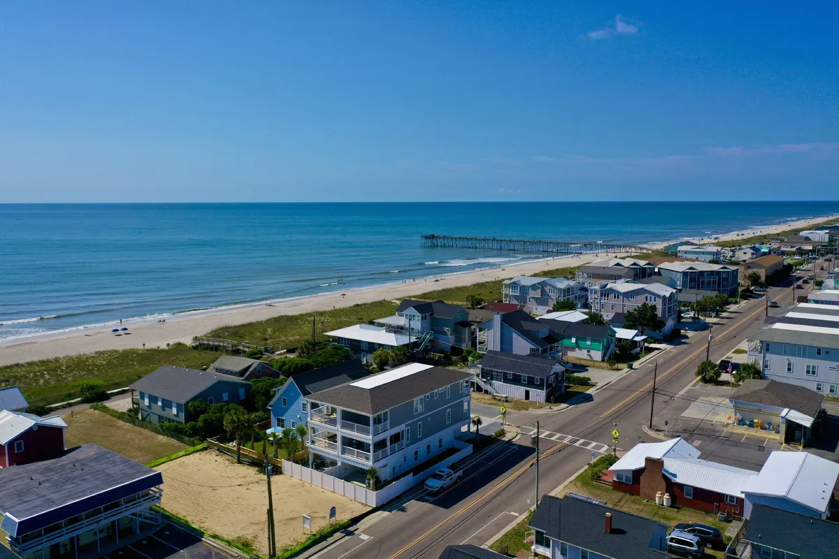A sweeping view of the beach, the ocean, the pier, and nearby houses, with a road leading into the heart of Kure Beach. The pier and shops are visible, inviting exploration and strolls during breaks.