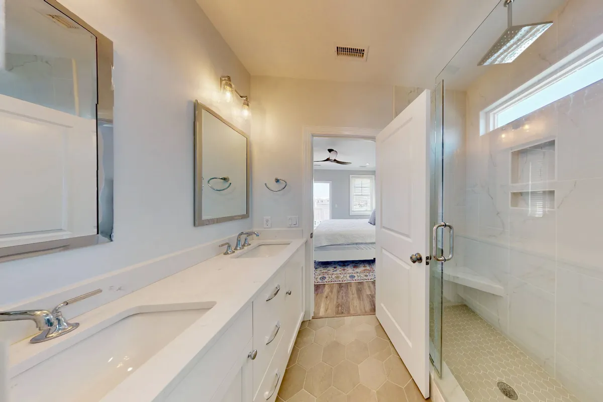 A modern, spa-inspired bathroom with a double sink vanity, glass shower enclosure, mirrored wall, and soft lighting fixtures. The room feels bright, inviting, and designed for rejuvenation and self-care.