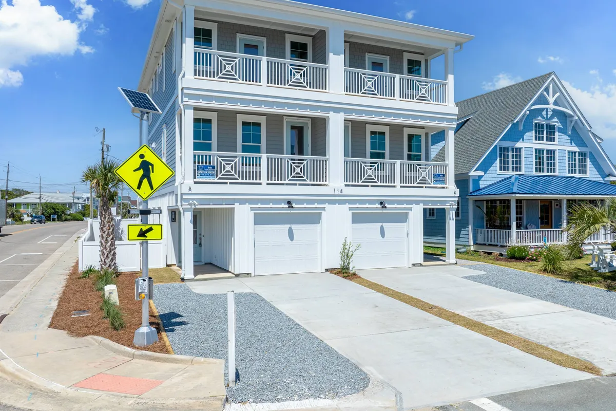 A bright exterior photo showcasing the two-story house with multiple balconies, palm trees, and walkway signs. The inviting porch and visible pathways reinforce easy access and a sense of community, while the house’s design reflects comfort and privacy.