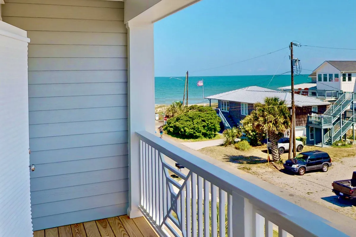 This exterior image provides a serene vantage point from a balcony or deck with a clear ocean view, nearby palm trees, and neighboring houses. The setting is ideal for enjoying morning coffee, watching sunsets, or hosting a barbecue with friends and family.