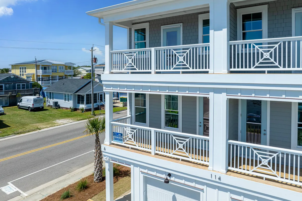 The image highlights the exterior of a duplex with balconies, a palm tree, and views of the street and neighboring homes. The balconies look inviting, suggesting outdoor relaxation and socializing in a cheerful setting.